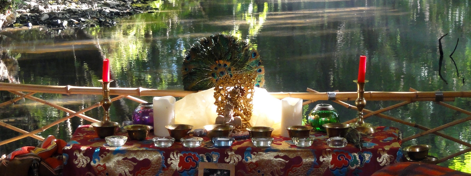 Buddhist shrine over a river with a feather fan, candles and light reflecting off the water