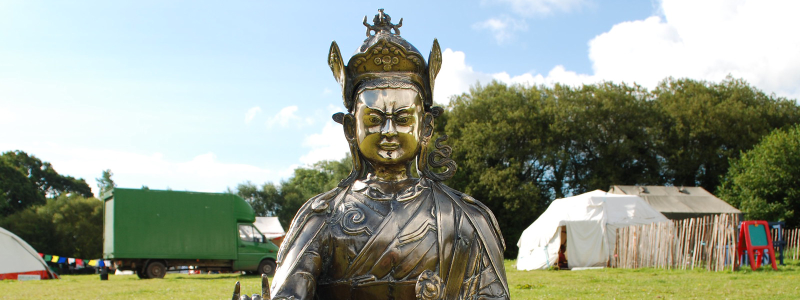 /buddhist Padmasambhava statue in front of a blue sky and some tents in a field